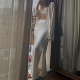 A woman stands on a balcony wearing a white satin maxi skirt and a matching shirt.