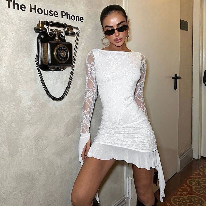 Woman in a white lace mini dress with long sleeves posing against a wall with a vintage phone