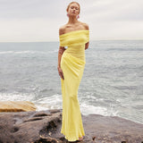 woman in yellow off-the-shoulder ruched dress standing on rocks by the sea