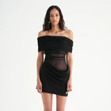 A woman wearing a black off-the-shoulder ruched dress with sheer panels and an asymmetrical hem.