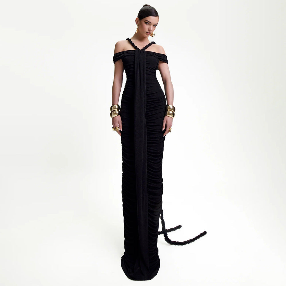 Model wearing a floor-length black ruched gown with off-the-shoulder sleeves and halter neck straps, accessorized with gold jewelry.