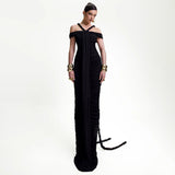 Model wearing a floor-length black ruched gown with off-the-shoulder sleeves and halter neck straps, accessorized with gold jewelry.