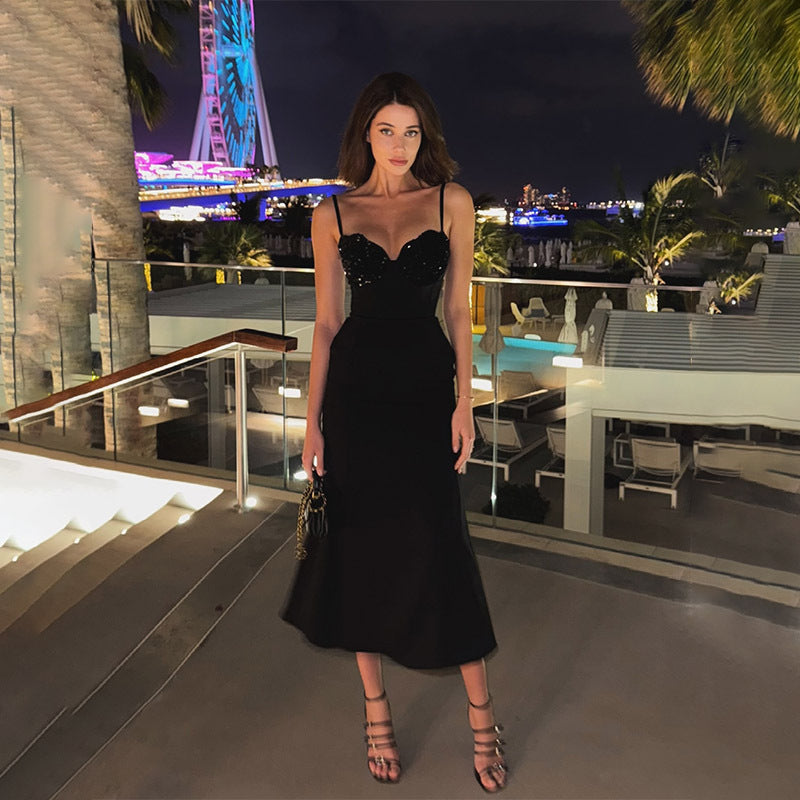 A woman in a black sequined midi dress poses on a balcony at night.