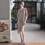 Woman in a champagne sequined dress with an asymmetrical hemline and flutter sleeves, holding a clutch
