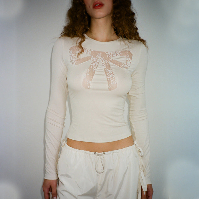 A woman wears a cream-colored long-sleeved shirt with a lace bow design on the chest and white drawstring pants.