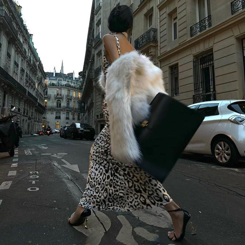 Woman walking away from the camera in a leopard print dress and faux fur coat on a European street.