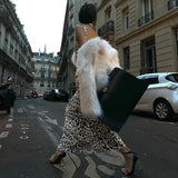 Woman walking away from the camera in a leopard print dress and faux fur coat on a European street.