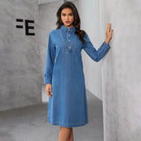 Woman in a long-sleeved denim dress posing against a wall.