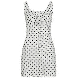 A white and black polka dot mini dress with a scoop neck and a tie-front detail lies flat.
