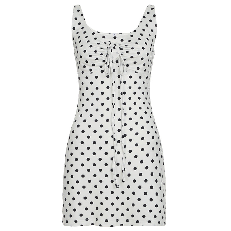 A white and black polka dot mini dress with a scoop neck and a tie-front detail lies flat.
