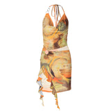 A sleeveless green, orange, and yellow abstract print mesh halter dress with a cowl neck, cut-out detail at the waist, a ring embellishment, and a ruched, asymmetrical hem.