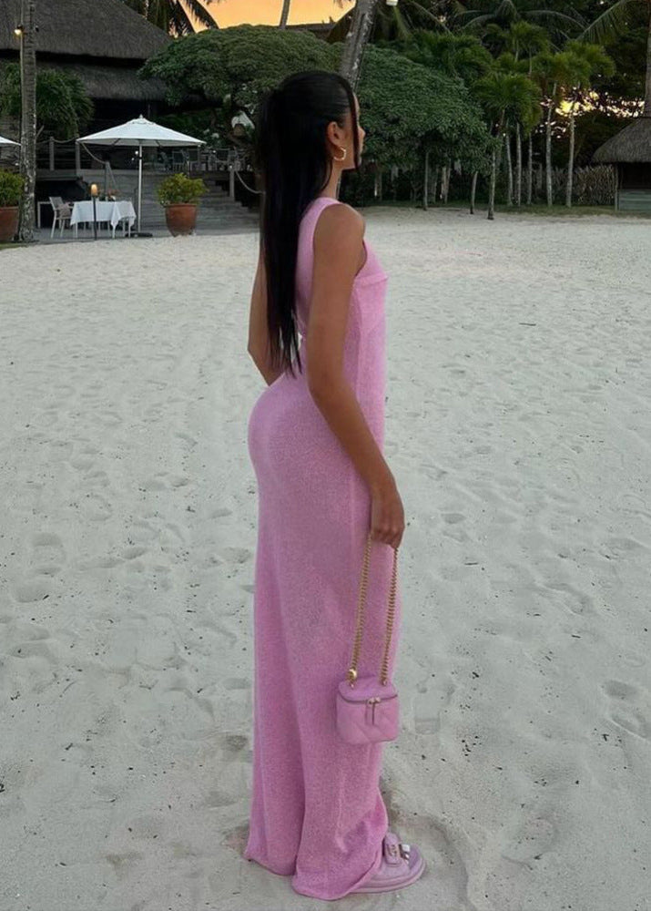 A woman in a pink knit maxi dress stands on a beach, viewed from the side.