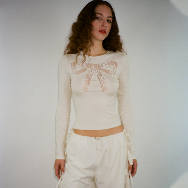 A woman wears a cream-colored long-sleeved shirt with a lace bow design on the chest and white drawstring pants.