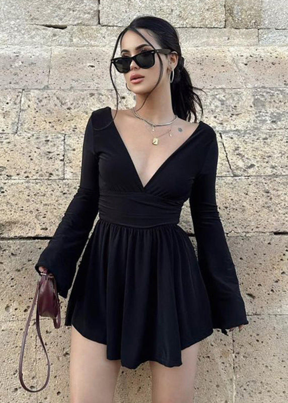 Woman wearing a black mini dress with flared sleeves and a deep V-neck, accessorized with sunglasses.