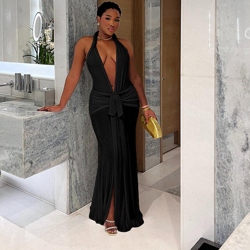 A woman in a long, black halter neck dress with a deep V-neck and a high slit, leaning against a bathroom counter.