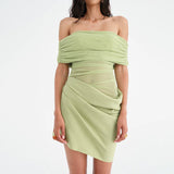 A mannequin wearing a light green off-the-shoulder ruched dress with sheer panels and an asymmetrical hem.
