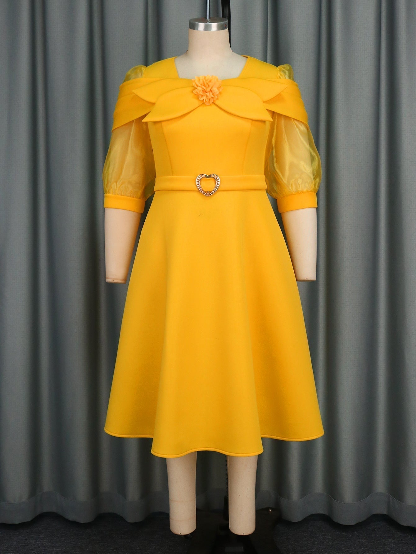 A yellow dress with sheer puffed sleeves and a floral detail at the neckline is displayed on a mannequin.