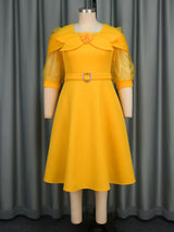 A yellow dress with sheer puffed sleeves and a floral detail at the neckline is displayed on a mannequin.
