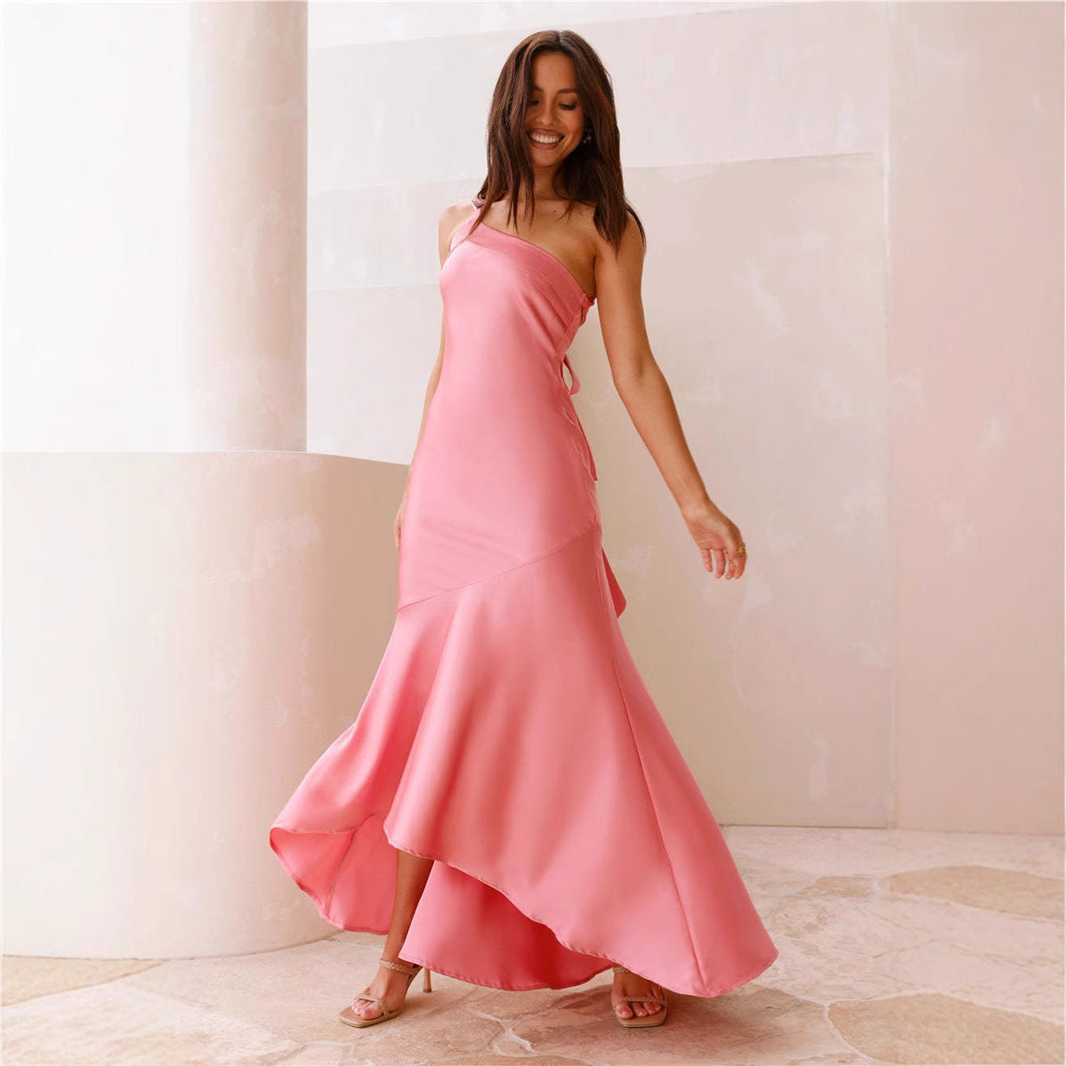 A woman in a flowing pink one-shoulder dress with an asymmetrical hemline, smiling and twirling.