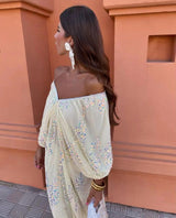 Close-up of a woman in a cream off-the-shoulder maxi dress with sequins, looking to the side.