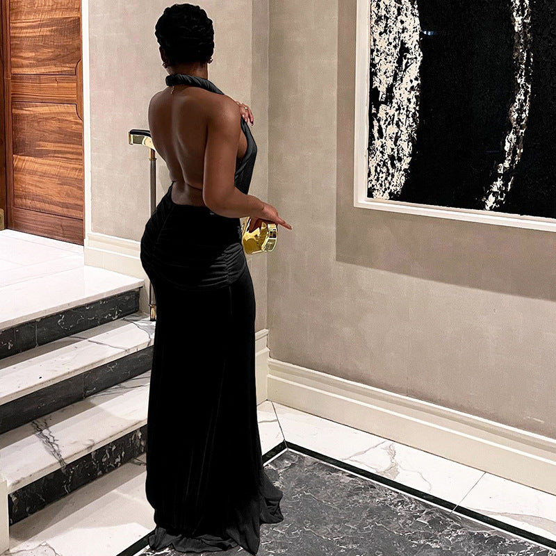 A woman in a long, black halter neck dress with a deep V-neck and a high slit, shown from the back, standing near a staircase.