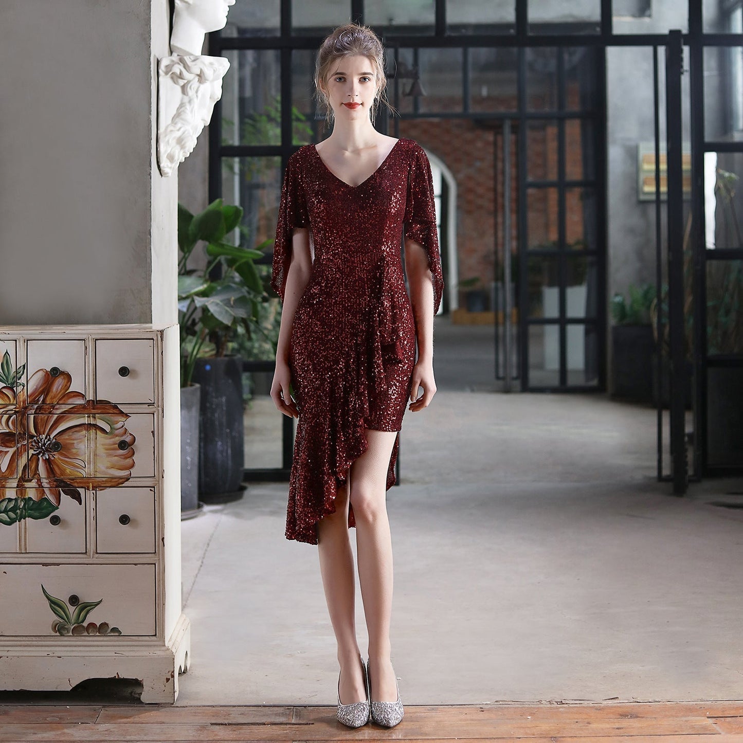 Woman in a burgundy sequined dress with an asymmetrical hemline and flutter sleeves