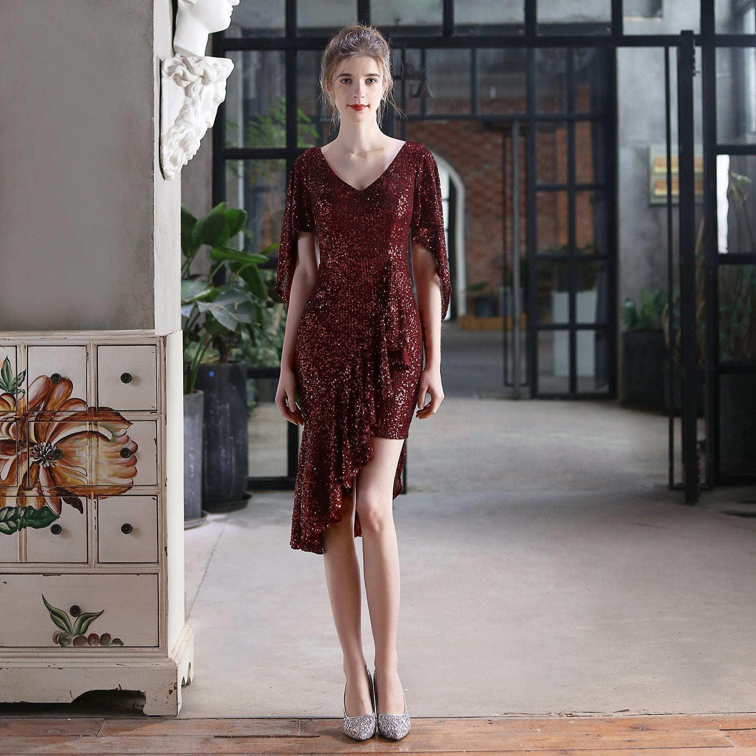 Woman in a burgundy sequined dress with an asymmetrical hemline and flutter sleeves