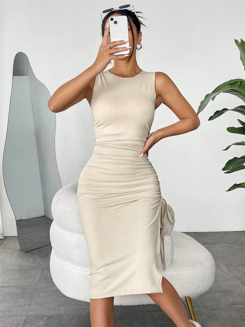 Woman in a beige ruched sleeveless midi dress, holding her phone and posing.