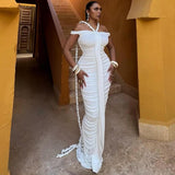 Woman posing in a white ruched gown with off-the-shoulder sleeves and halter neck straps, with a braided rope detail trailing.