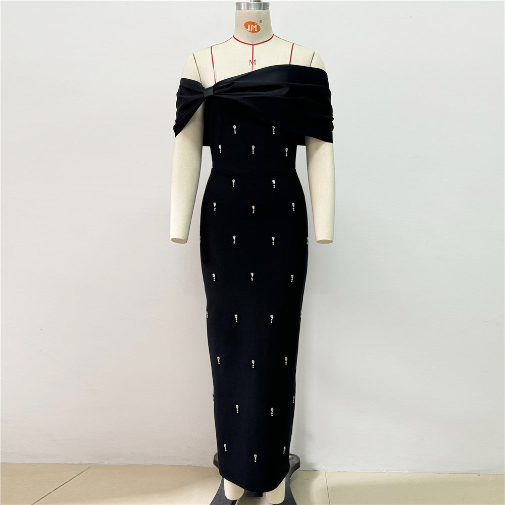 A black off-the-shoulder gown with a draped bodice and a bow detail, embellished with small white accents, displayed on a mannequin.
