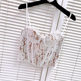 White lace corset top with tan lining, hanging on a black hanger against a white slatted background.