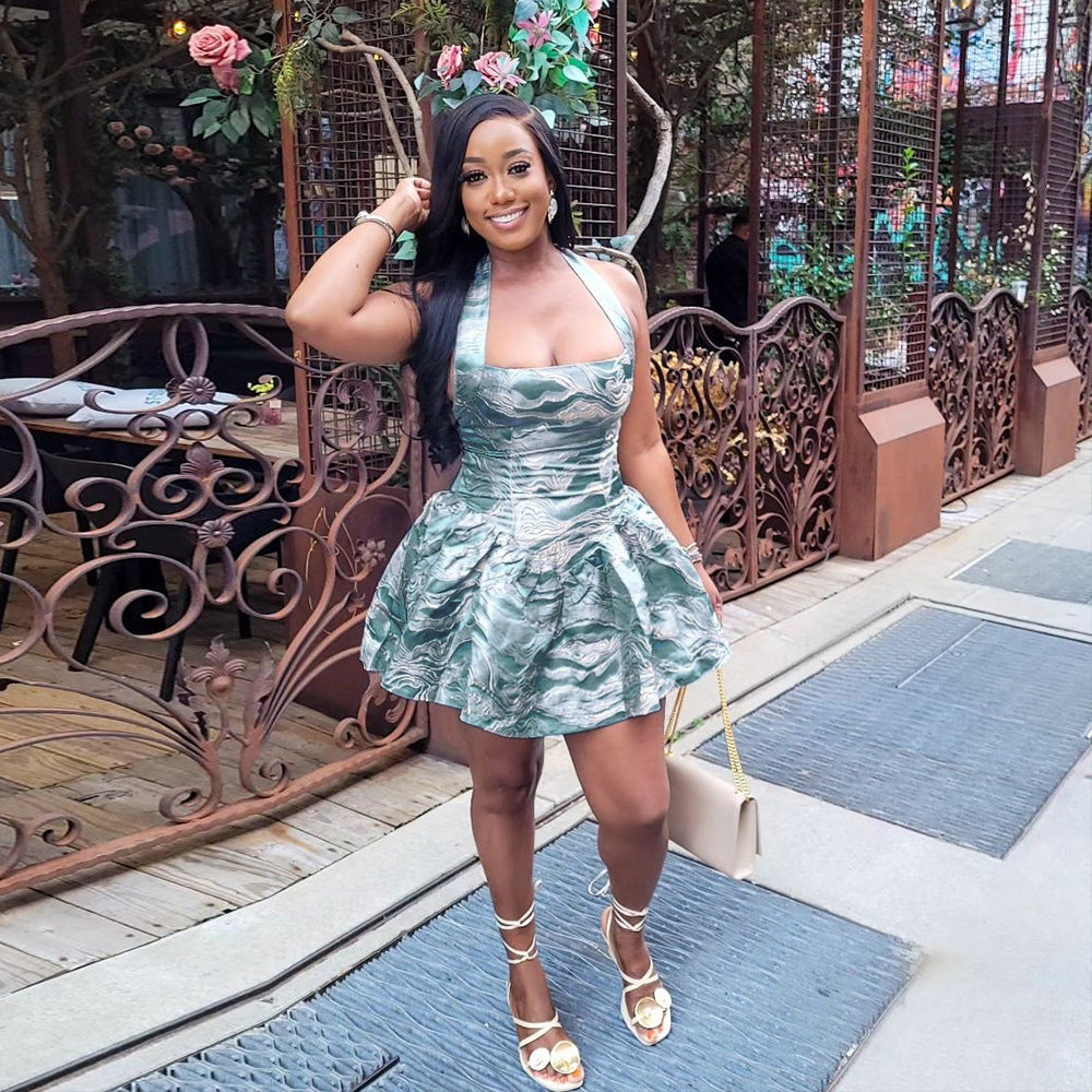 A woman in a green halter dress with a pleated skirt and white strappy heels smiles at the camera.