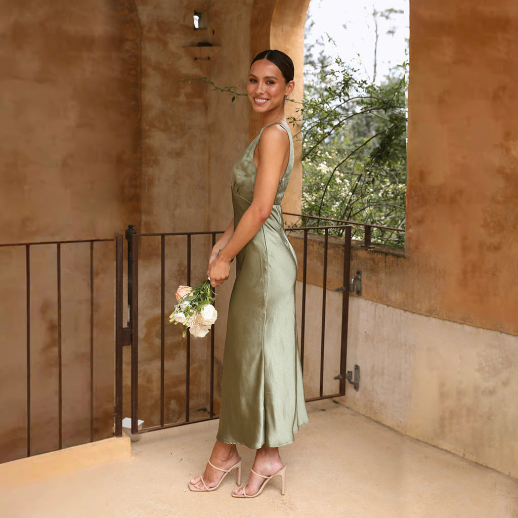 Woman in a sage green satin slip dress holding a bouquet of flowers, leaning on a railing on a balcony.