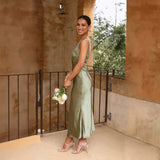 Woman in a sage green satin slip dress holding a bouquet of flowers, leaning on a railing on a balcony.