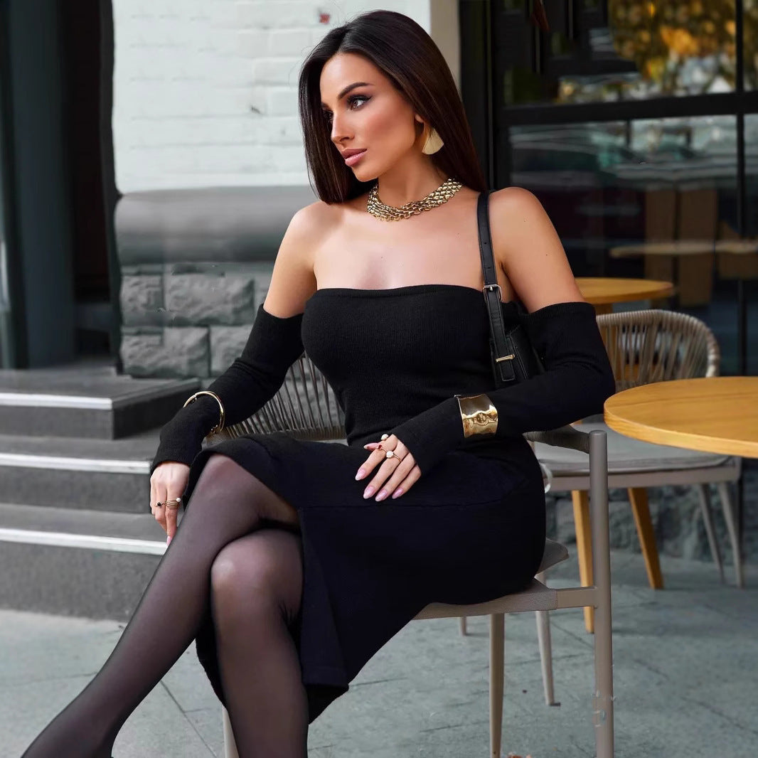 A woman in a black off-the-shoulder midi dress sits at an outdoor cafe table.
