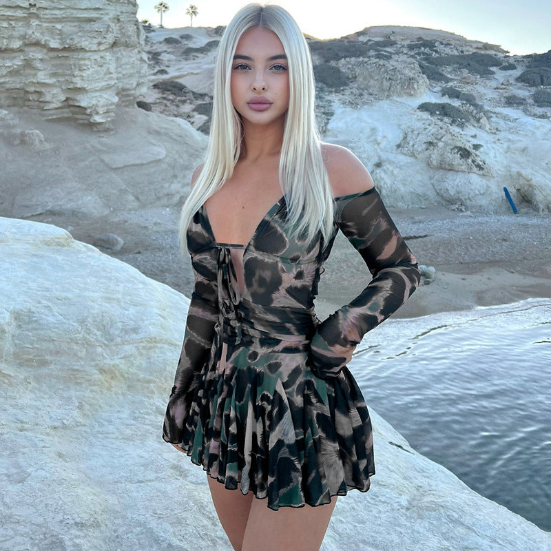 woman in a short dress with a camouflage print standing on rocks by the sea