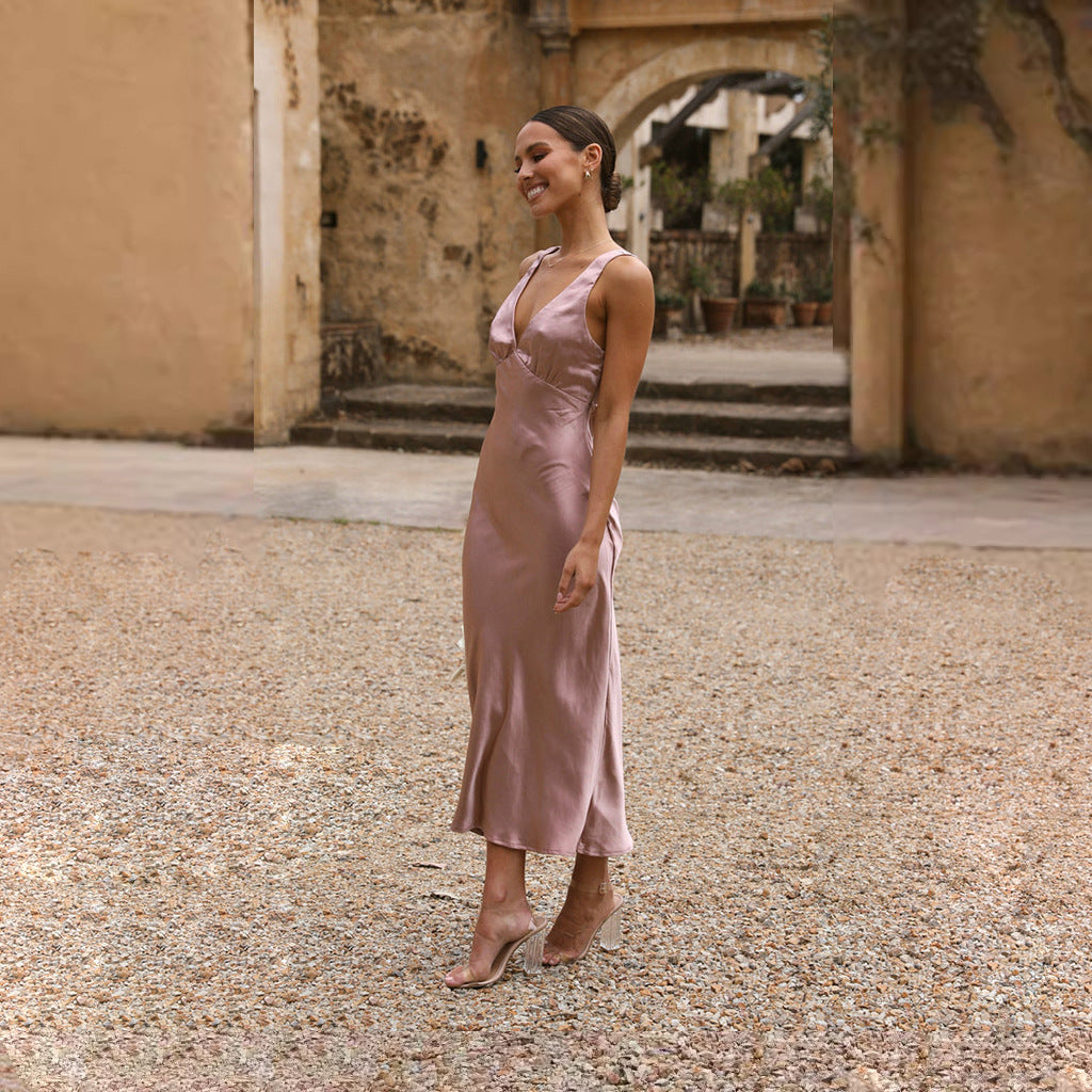 Woman in a pink satin slip dress holding a bouquet of flowers, standing outdoors and smiling.