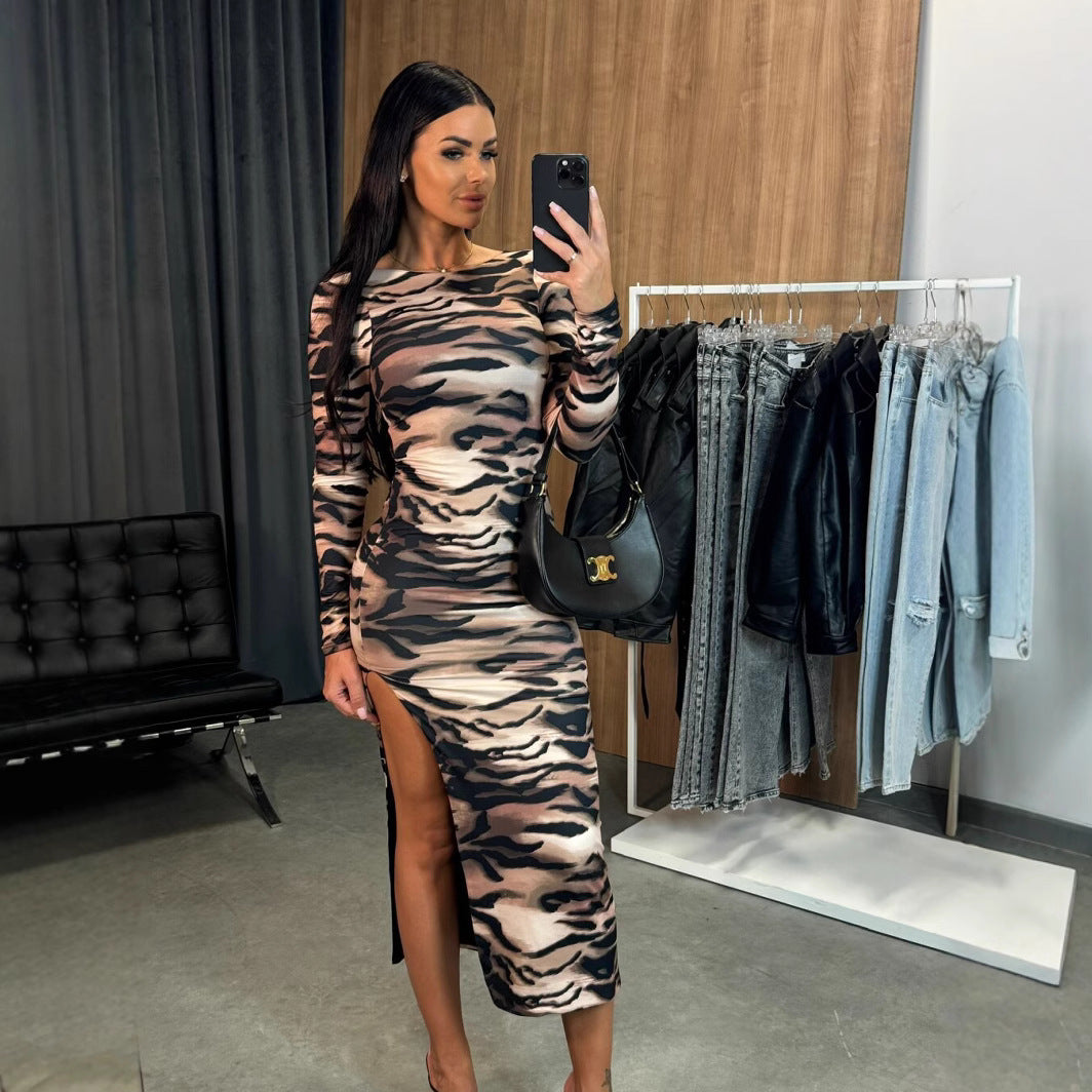 Woman in a long-sleeved tiger print dress with a high slit, holding a black handbag and taking a selfie.