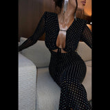 Close-up of a woman wearing a black sparkly dress with a plunging neckline and long sleeves.