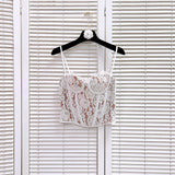 White lace corset top with tan lining and adjustable straps, displayed on a black hanger with a white floral embellishment.