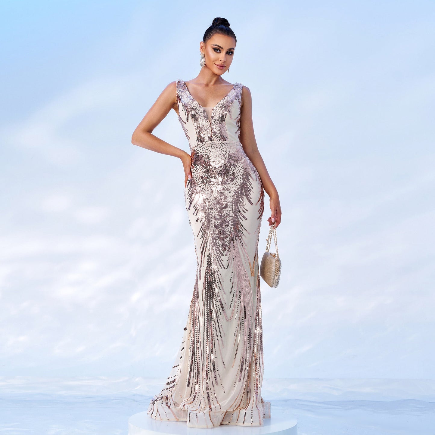Woman in a champagne and rose gold sequined mermaid gown with a v-neck and sleeveless design, holding a clutch.