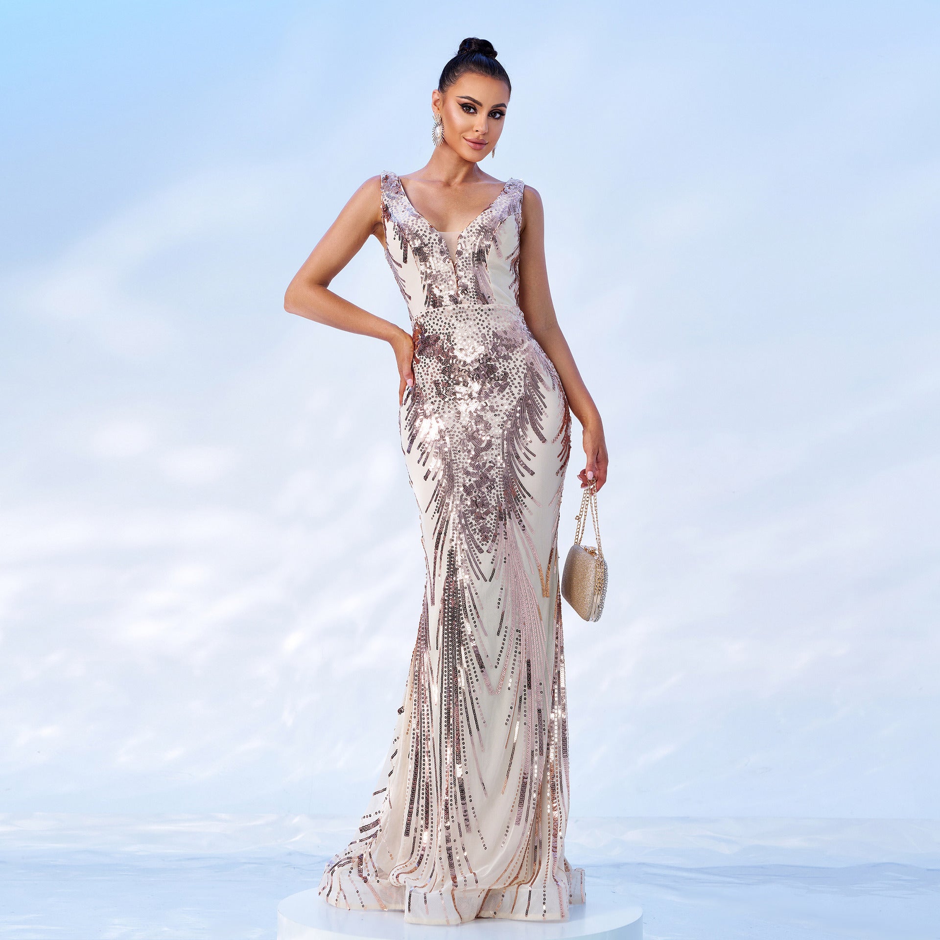 Woman in a champagne and rose gold sequined mermaid gown with a v-neck and sleeveless design, holding a clutch.