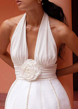 Close-up of a white halter neck dress with a deep V-neckline and a rose embellishment at the waist, showing the pearl detailing.