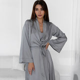 Woman in a grey satin robe tied at the waist, posing with one hand on her hip.