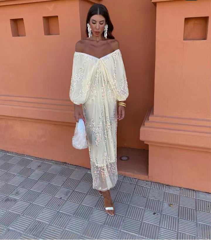 Woman in a cream off-the-shoulder maxi dress with sequins and long sleeves.