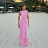 A woman in a pink maxi dress stands on a beach.