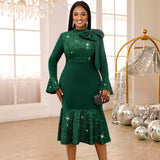 A woman in a green sequined dress with bell sleeves and a bow at the neck.