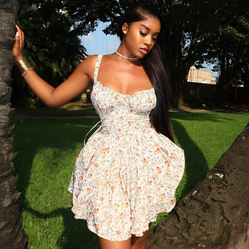 A young Black woman stands between two palm trees, wearing a floral sundress.
