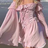 Woman wearing a pink off-the-shoulder dress with a corset bodice and bell sleeves on the beach