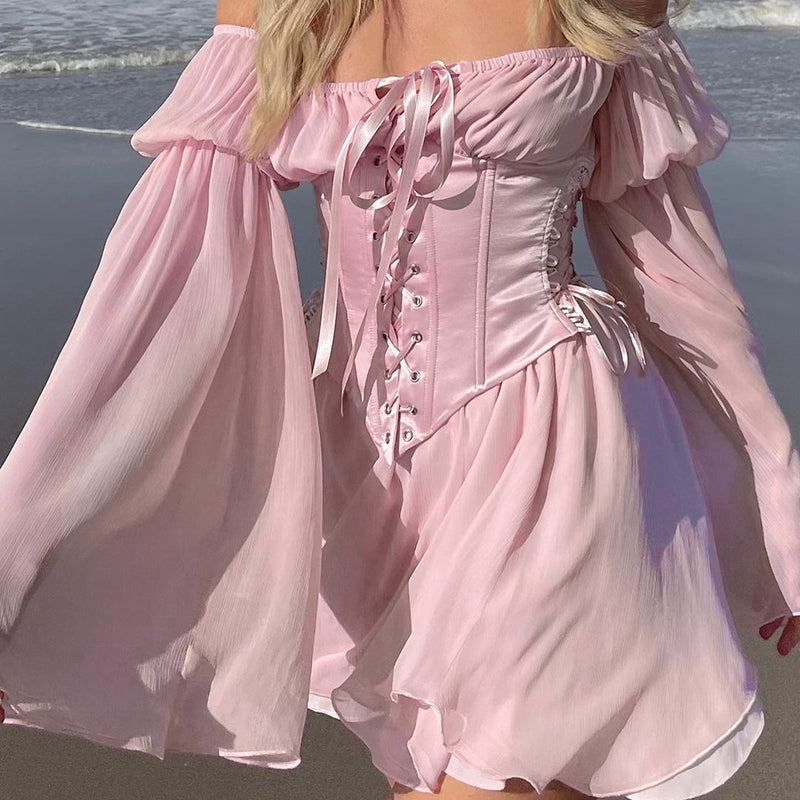Woman wearing a pink off-the-shoulder dress with a corset bodice and bell sleeves on the beach